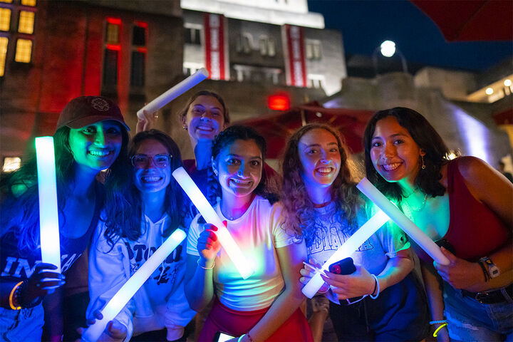 A diverse group of university students holding glow sticks outside the Indiana Memorial Union Building.